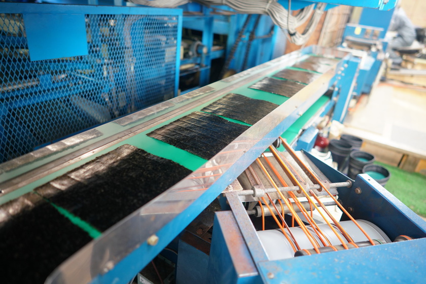 The finished nori come out of a huge machine in full-size sheets, in which they are shaped and dried, moving rhythmically.